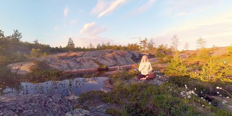 A woman sits in a rocky field at sunset cross-legged.