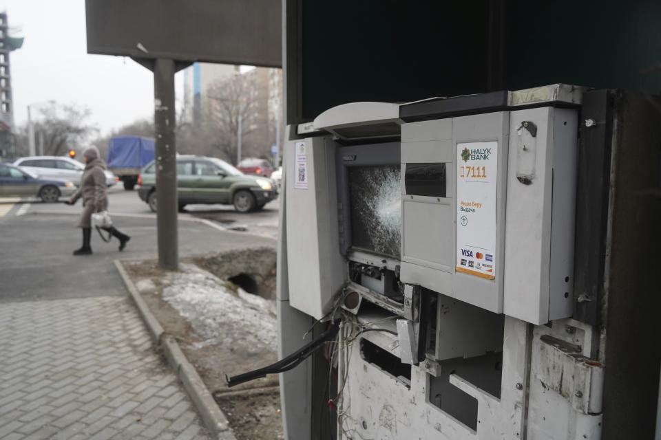 A woman walks past an ATM machine damaged during clashes on the street in Almaty, Kazakhstan, Tuesday, Jan. 11, 2022. Life in Almaty, which was affected with the violence the most, started returning to normal this week, with public transport resuming operation and malls reopening. (Vladimir Tretyakov/NUR.KZ via AP)