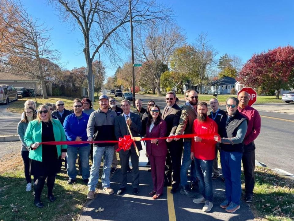 Muncie Mayor Dan Ridenour, with scissors, and Elizabeth Rowray, President of the Delaware Advancement Corporation, right of Ridenour, are among local officials who cut the ribbon in November, celebrating the completion the Riverside trail project. The project grew into a repaving of the westside street and drainage repair for the residential area.