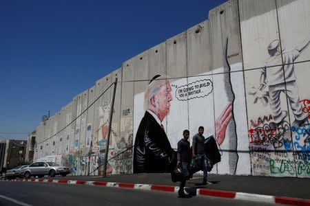 Palestinians walk past a graffiti depicting U.S President Donald Trump on the controversial Israeli barrier in the West Bank town of Bethlehem August 4, 2017. REUTERS/Mussa Qawasma