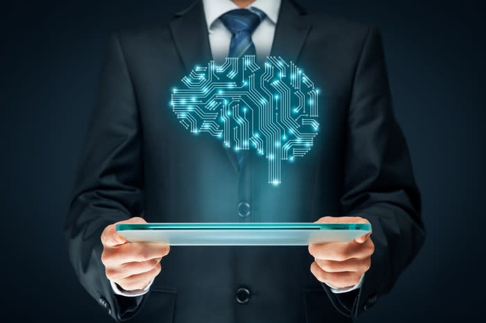 A man in a suit holding a tablet. An illustrated brain made of electrical connections hovers above the tablet, signifying artificial intelligence.