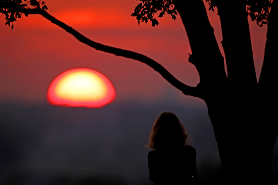 FILE - In this July 3, 2020, file photo, a woman watches the sunset from a park in Kansas City, Mo. 2020 is barely halfway over. That hasn't stopped many people from declaring the year canceled and wishing it would end. (AP Photo/Charlie Riedel, File)