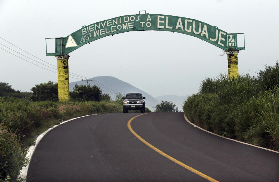 In this Oct. 16, 2019 photo, a sign arches over a two lane road welcoming vistors to El Aguaje, Mexico. Michoacan state police did make a rare appearance in El Aguaje last Monday, Oct. 14, they were ambushed and slaughtered by Jalisco cartel gunmen. (AP Photo/Marco Ugarte)