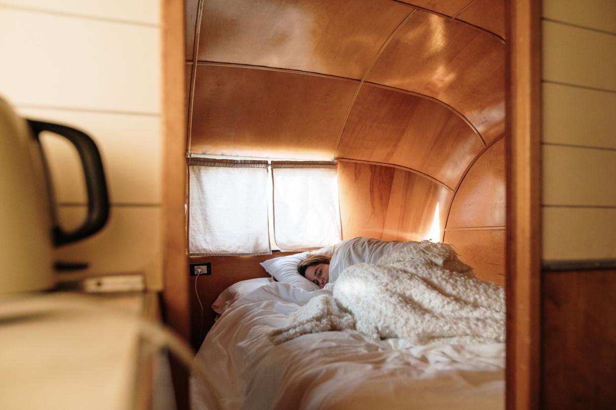 A young woman sleeping on a cozy bed inside a vintage camper trailer