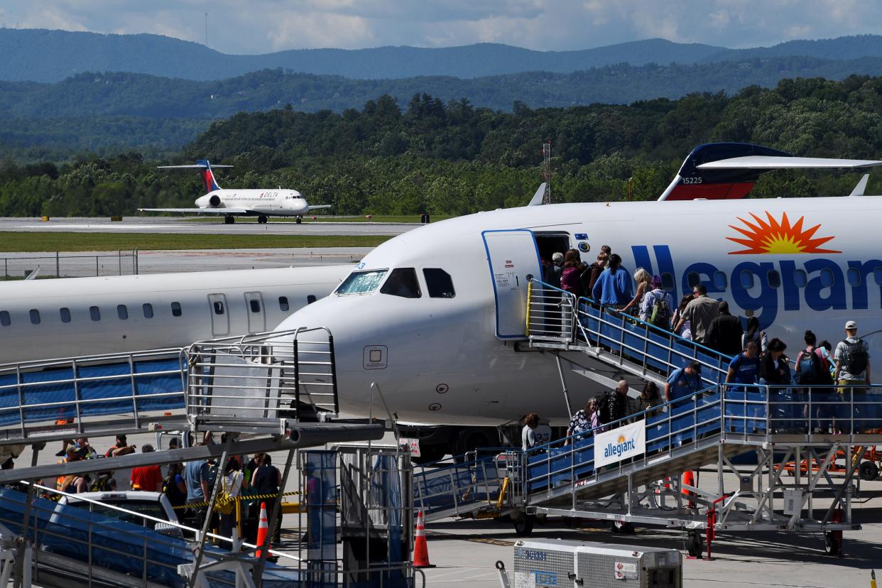 Travelers wait in line to board an Allegiant flight at Asheville Regional Airport as a Delta flight prepares for takeoff, June 7, 2024.