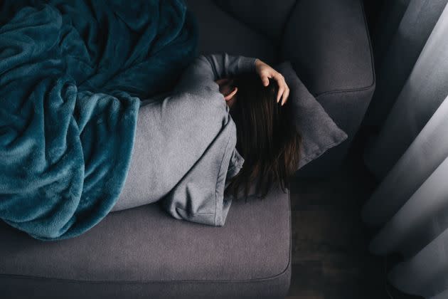 Frustrated depressed millennial girl lying in embryo pose on couch, sleeping, drowsing, feeling stress, apathy, suffering from abdominal pain, bellyache. Depression concept. Top view