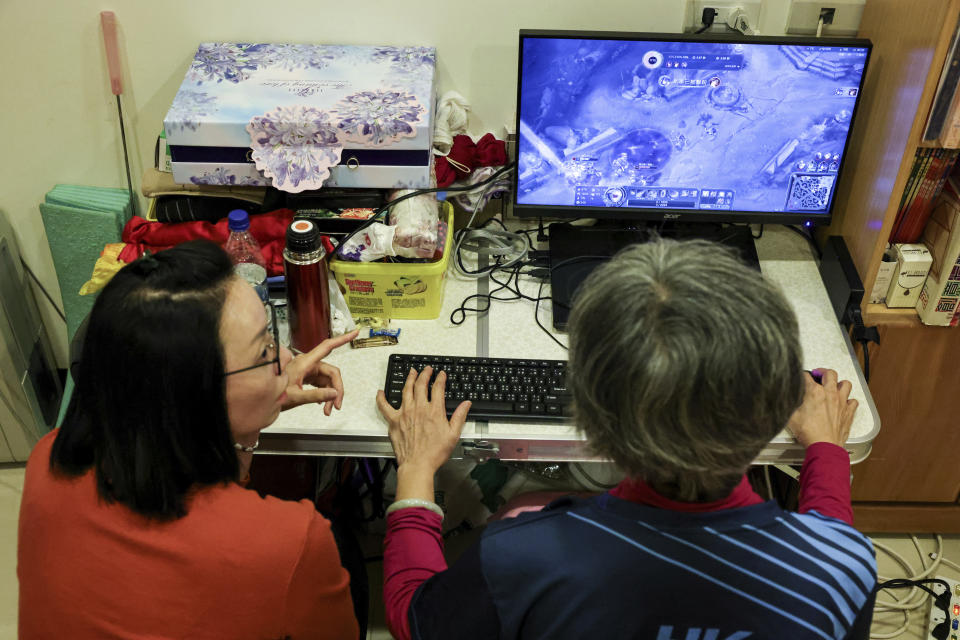 Sixty five-year-old esport player Chiang Yi-Shu, right, practices at home while explaining the game to her daughter Liang Ying-Fang, left, in New Taipei city, Taiwan on Friday, Dec. 16, 2022. Chiang is one of the League of Legends players on Hungkung Evergreen Gaming's team, established this summer. The team, whose members range from 62 to 69 years old, was founded by Huang Jianji, the director of the department of Multimedia Game development and application of Hungkuang University. They competed in their first-ever video game tournament Saturday at the university. (AP photo/I-Hwa Cheng)