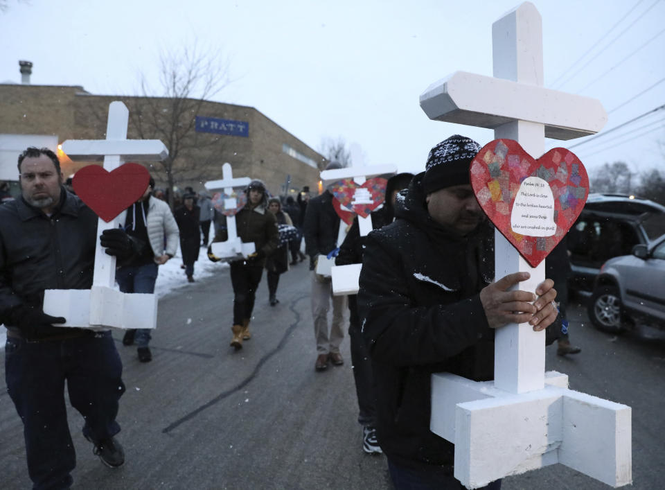Casildo Cuevas, right, holds a victim's cross as he walks to the Aurora police station after a makeshift memorial Sunday, Feb. 17, 2019, in Aurora, Ill., near Henry Pratt Co. manufacturing company where several were killed on Friday. Authorities say an initial background check five years ago failed to flag an out-of-state felony conviction that would have prevented a man from buying the gun he used in the mass shooting in Aurora. (AP Photo/Nam Y. Huh)