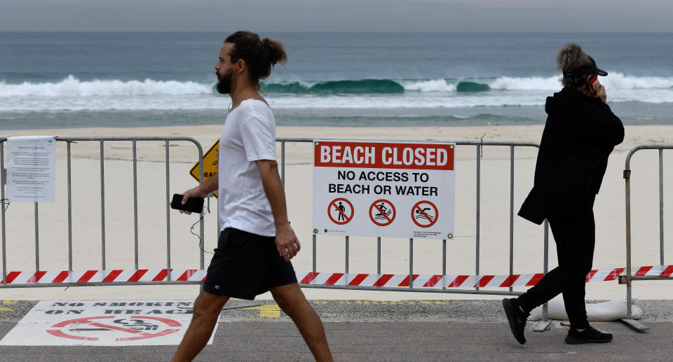 People are seen walking along Bondi Beach in Sydney past a 'beach closed' sign.