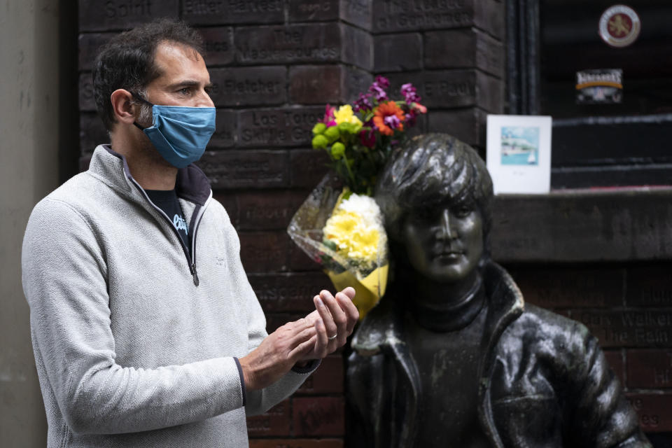 A member of the entertainment industry stands by a statue of John Lennon in Liverpool, England, Monday Oct. 12, 2020, during a show of support for the hard hit sector as Prime Minister Boris Johnson lays out a new three-tier alert system for England. The British government is set to announce new restrictions on business and socializing in major northern England cities with high infection rates, under a plan to put areas into three tiers. (AP Photo/Jon Super)