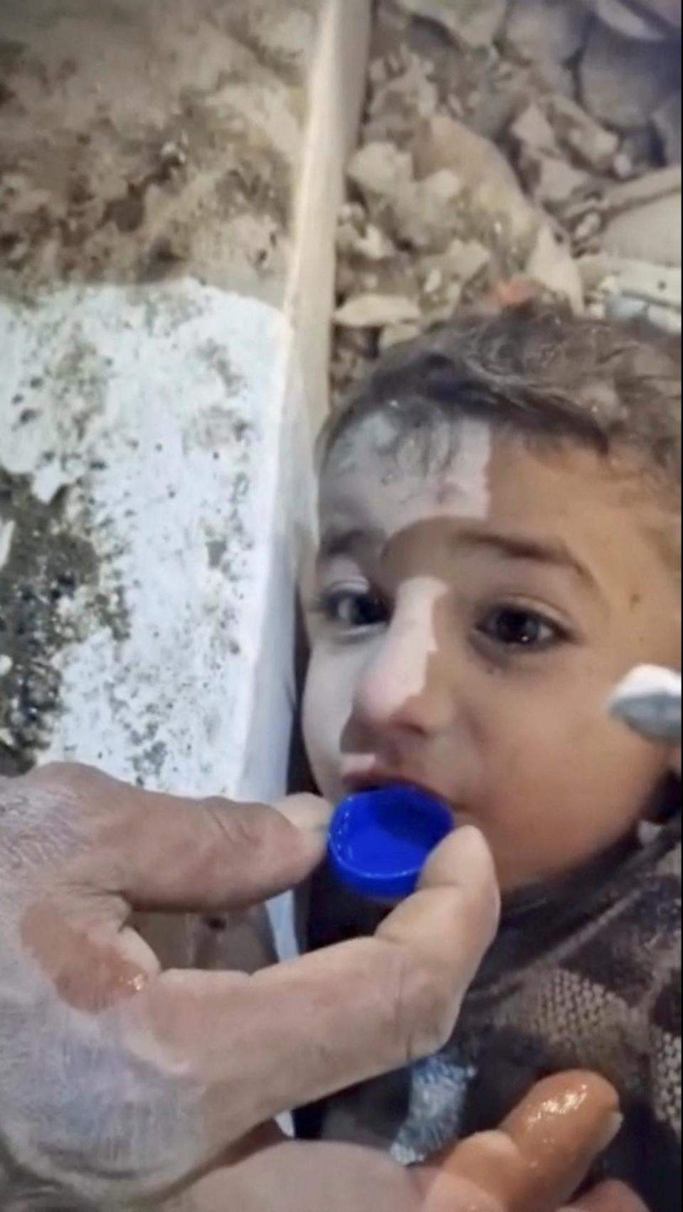 Rescuers give a boy water in a bottle cap as they rescue him from the rubble following an earthquake in Hatay, Turkey (via REUTERS)