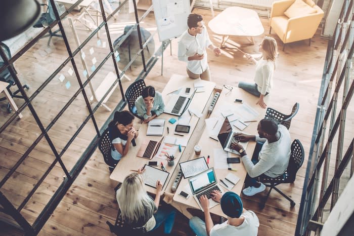 A group of people sitting around a long table work at computers.