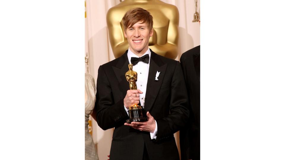 Dustin Lance Blakc in a tuxedo holding an Oscar award