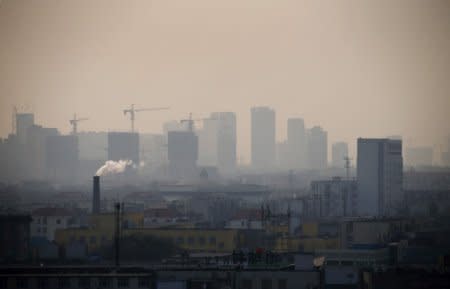 FILE PHOTO: Smoke rises from a chimney among houses as new high-rise residential buildings are seen under construction on a hazy day in the city centre of Tangshan, Hebei province in this February 18, 2014 file photo.   REUTERS/Petar Kujundzic/File Photo