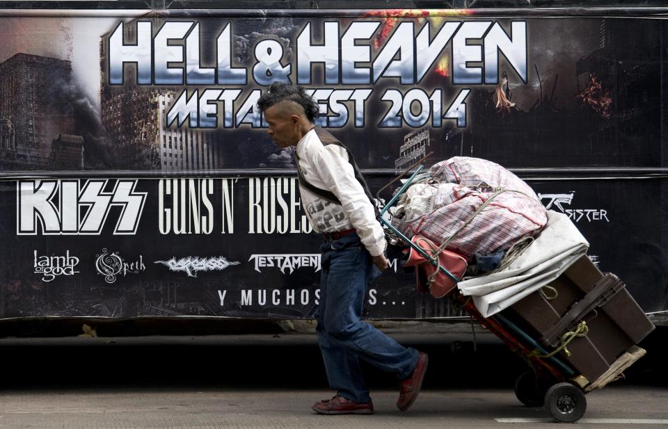 A man pulls a dolly loaded with supplies past publicity of "Hell and Heaven Metal Fest" concert, posted on bus in Mexico City, Friday March 7, 2014. The Mexico state government canceled the concert saying the March 15-16 "Hell and Heaven Metal Fest" planned for a fairground just east of Mexico City did not have adequate safety plans, posing a risk to concert-goers. (AP Photo/Eduardo Verdugo)