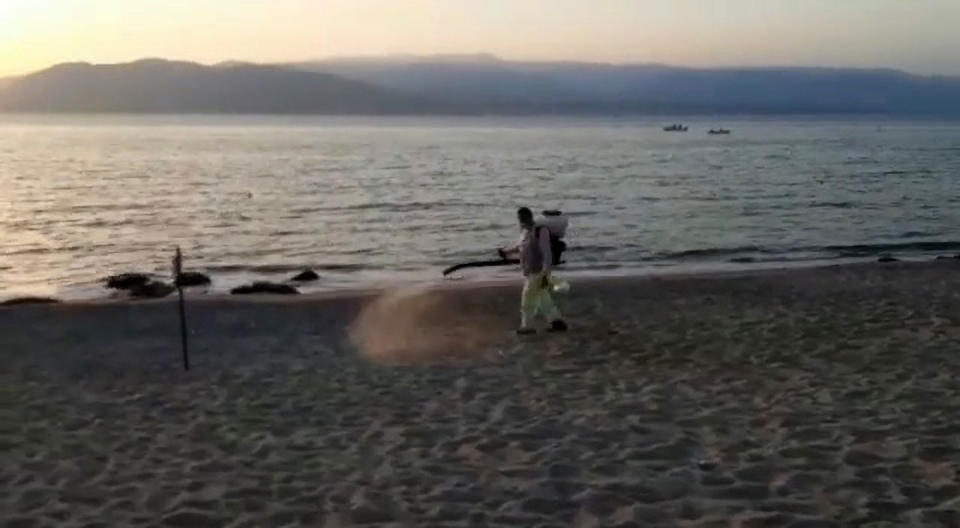 A council worker in a protective suit using a disinfectant sprayer on the beach.