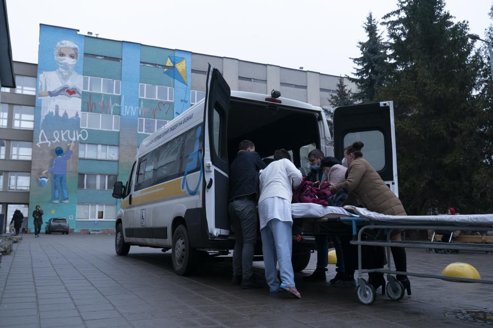 Medical workers transfer a coronavirus patient from an ambulance to a hospital organized in the medical college in Lviv, Western Ukraine, on Monday, Jan. 4, 2021. A medical college in western Ukraine has been transformed into a temporary hospital as the coronavirus inundates the Eastern European country. The foyer of the college in the city of Lviv holds 50 beds for COVID-19 patients, and 300 more were placed in lecture halls and auditoriums to accommodate the overflow of people seeking care at a packed emergency hospital nearby. (AP Photo/Evgeniy Maloletka)