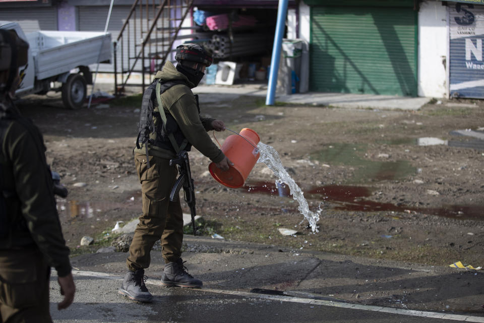 An Indian soldier washes blood stains on a road at the site of an attack on the outskirts of Srinagar, Indian controlled Kashmir, Thursday, March 25, 2021. Rebels fighting against Indian rule in disputed Kashmir Thursday attacked a paramilitary patrol, killing two soldiers and injuring two others, an official said. (AP Photo/Mukhtar Khan)