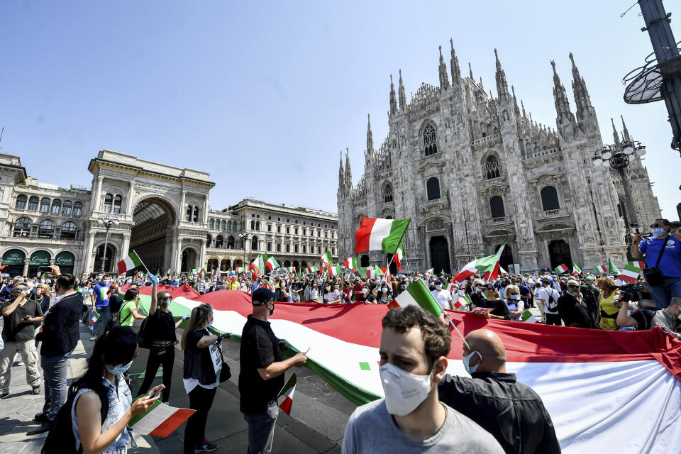 People hold a giant Italian flag as they stage an anti-government protest set by the center-right opposition, in front of Milan gothic cathedral, Italy, Tuesday, June 2, 2020 on the day marking the 74th anniversary of the Italian Republic. (Claudio Furlan/LaPresse via AP)