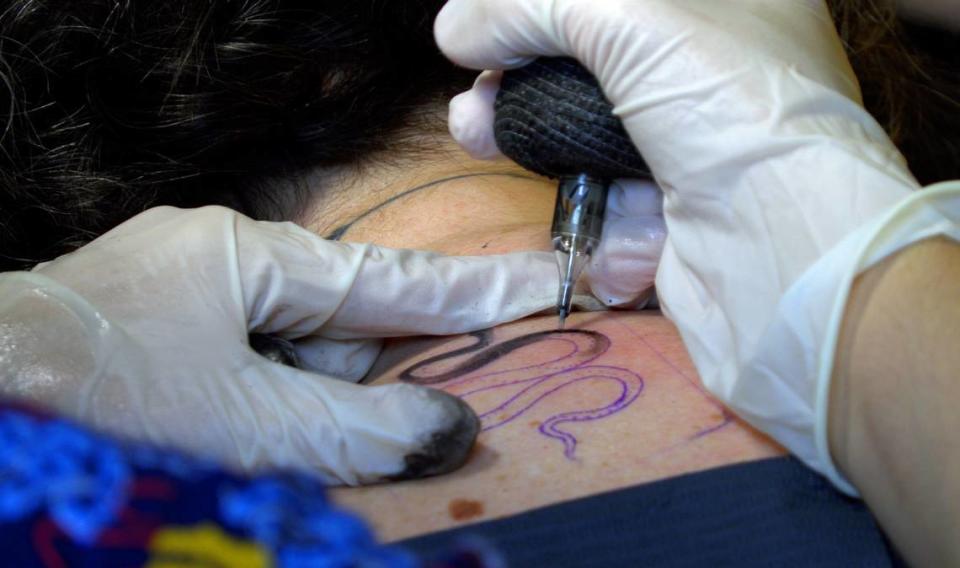 Van Bixler, a tattoo artist at Smoking Mirror Tattoo Gallery in Columbus, Georgia, adds a tattoo of a small snake to Ledger-Enquirer reporter Sundi Rose’s upper back.