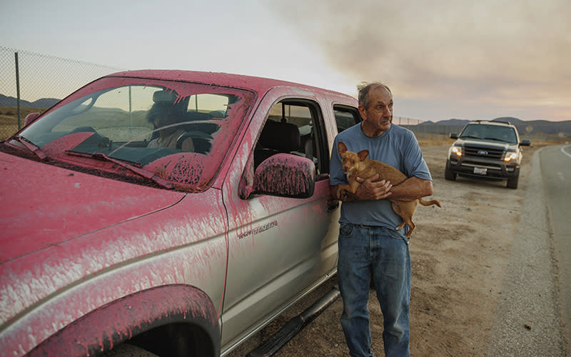 A man holds a dog after evacuating from a wildfire