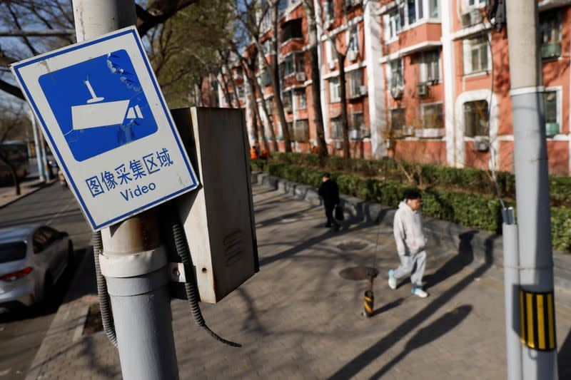 A sign notifying the area is under video surveillance is pictured in a pole while people walk on a street in Beijing