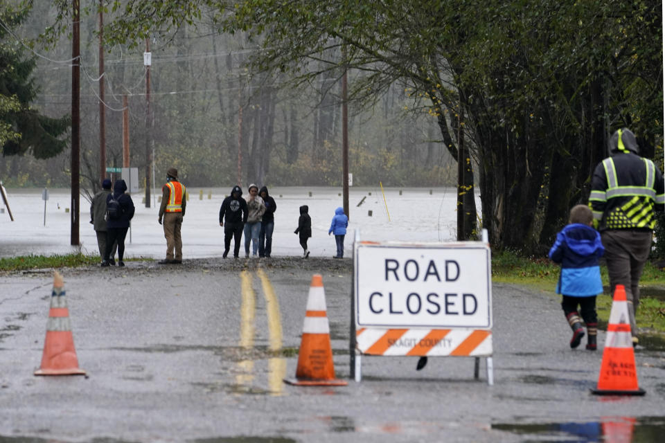 Locals walk up to a roadway flooded from the overflowing Skagit River, Monday, Nov. 15, 2021, in Sedro-Woolley, Wash. (AP Photo/Elaine Thompson)