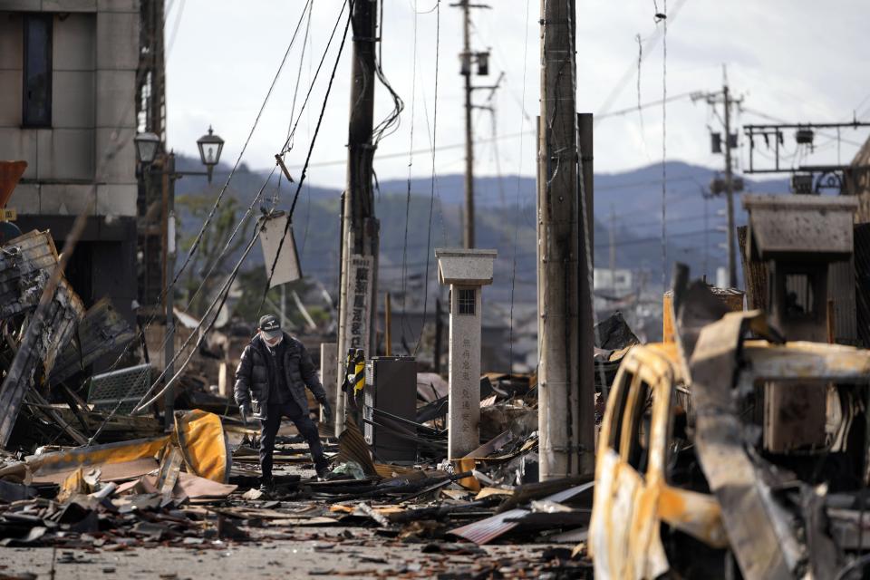 A man walks through debris after a fire at a shopping area in Wajima in the Noto peninsula, facing the Sea of Japan, northwest of Tokyo, Friday, Jan. 5, 2024, following Monday's deadly earthquake. (AP Photo/Hiro Komae)