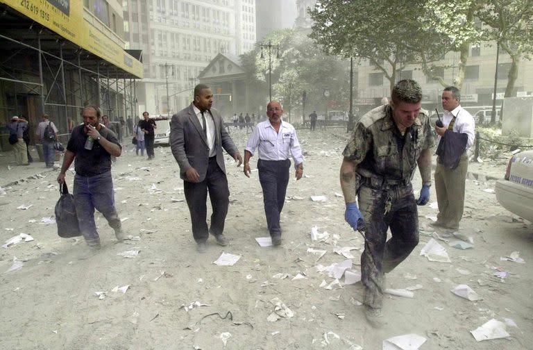 Un oficial de polic&#xed;a y varios ciudadanos caminan por las calles cubiertas de escombros cerca de las torres del World Trade Center