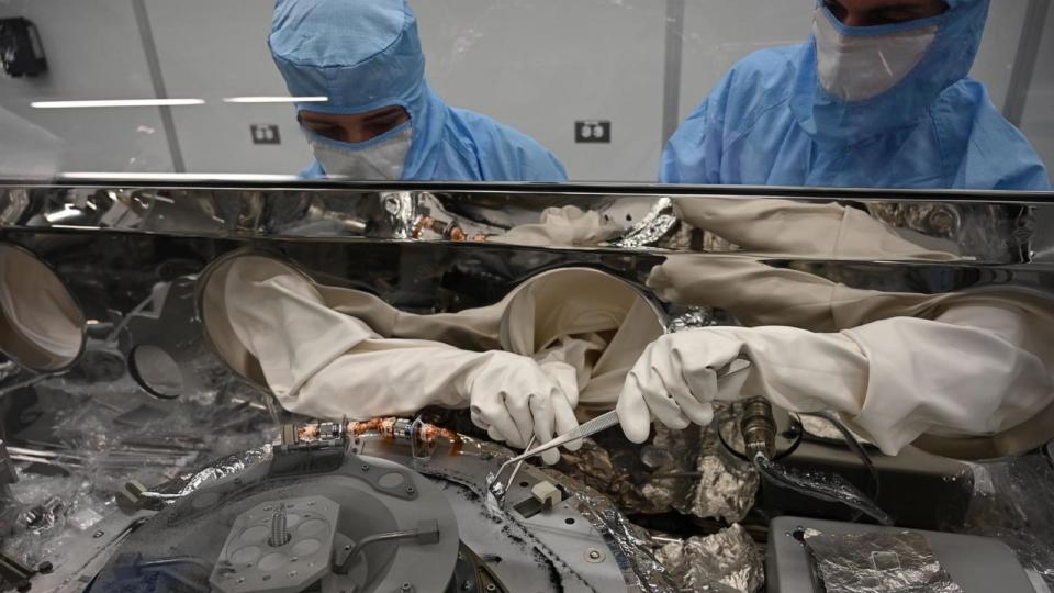 PHOTO: Astromaterials processors Mari Montoya, left, and Curtis Calva, right, use tools to collect asteroid particles from the base of the OSIRIS-REx science canister, Sep. 27, 2023. (NASA)