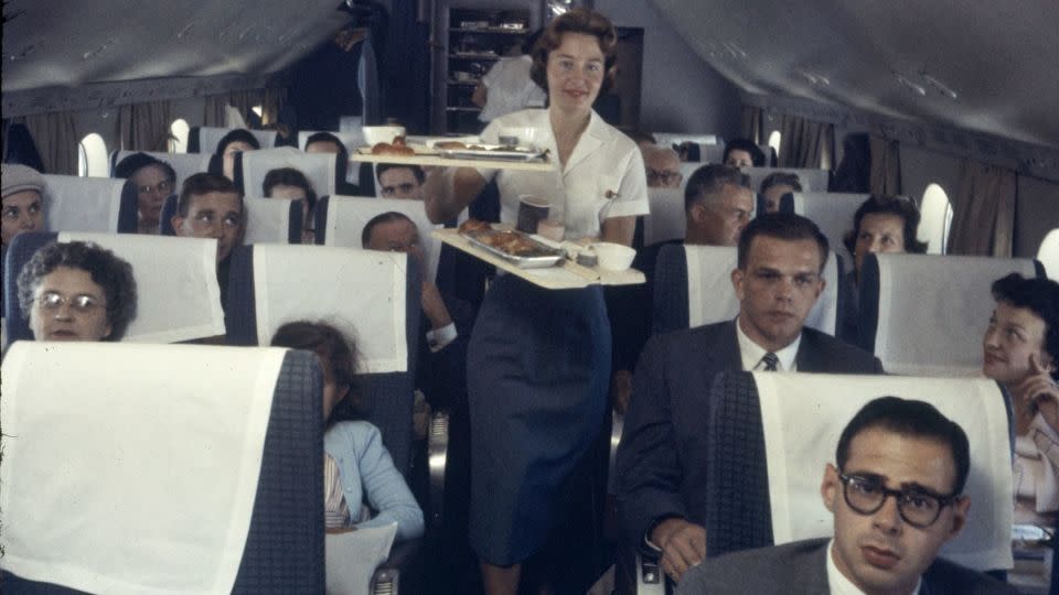 A Pan American Airline flight attendant serves trays of food to passengers on a plane in 1958. - Peter Stackpole/The LIFE Picture Collection/Shutterstock