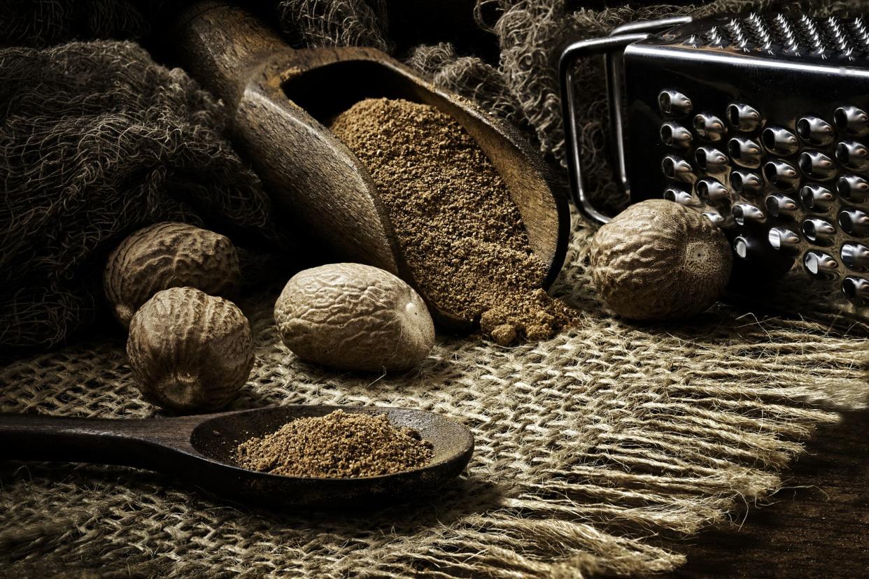 Close-up of whole nut and nutmeg powder in a wooden spoon with  on burlap and rustic table