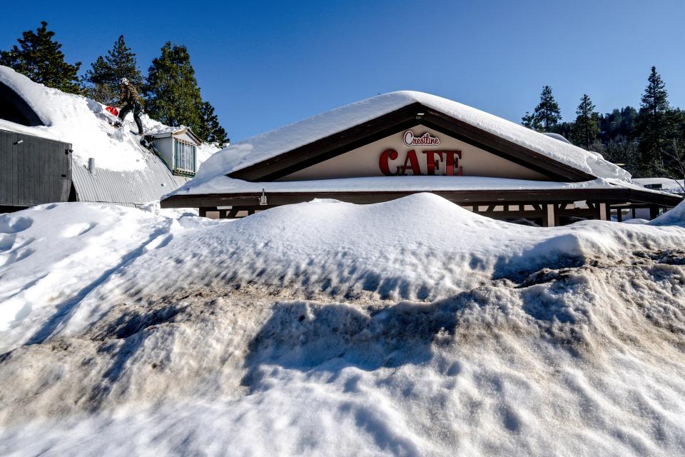 A man shovels snow off the roof of a store in Crestline, Calif., on March 3, 2023, as buildings remain buried in several feet of snow from recent winter storms.