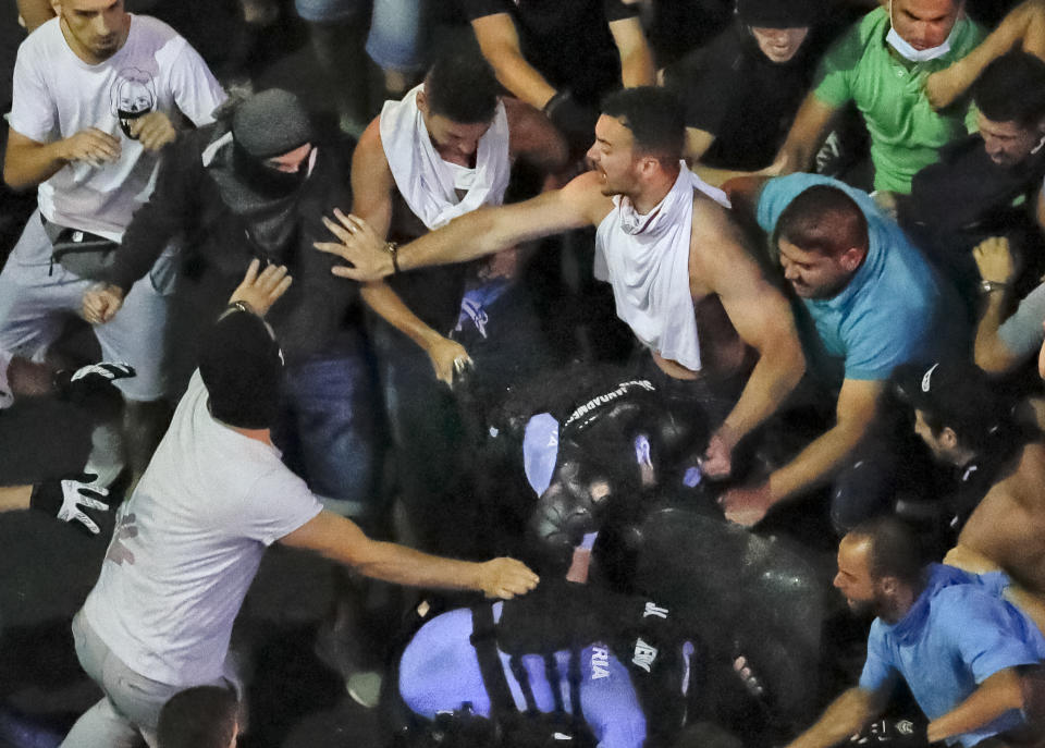 In this Friday, Aug. 10, 2018, photo, a man attempts to remove the handgun from a female riot police officer after she and a colleague fell, were left behind and ended up mobbed by people during a charge to clear the square during protests outside the government headquarters, in Bucharest, Romania. Romanian authorities say hundreds of people including two dozen riot police have received medical treatment after an anti-government protest turned violent and two weapons were stolen from riot police officers. (AP Photo/Vadim Ghirda)