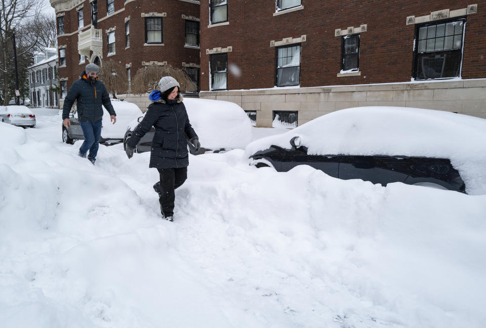 Joseph McVay, left, and Sarah Guglielmi who live nearby, walk along a street in the Elmwood Village neighborhood of Buffalo, N.Y. Monday, Dec. 26, 2022, after a massive snow storm blanketed the city. Along with drifts and travel bans, many streets were impassible due to abandoned vehicles. (AP Photo/Craig Ruttle)