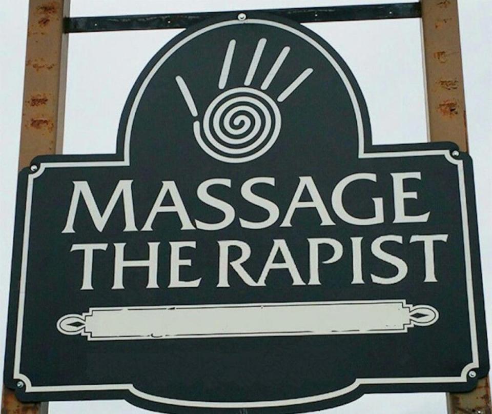 An outdoor sign that reads "Massage the rapist" with a decorative hand symbol at the top; there's some very unfortunate spacing going on (it's supposed to read Massage Therapist)