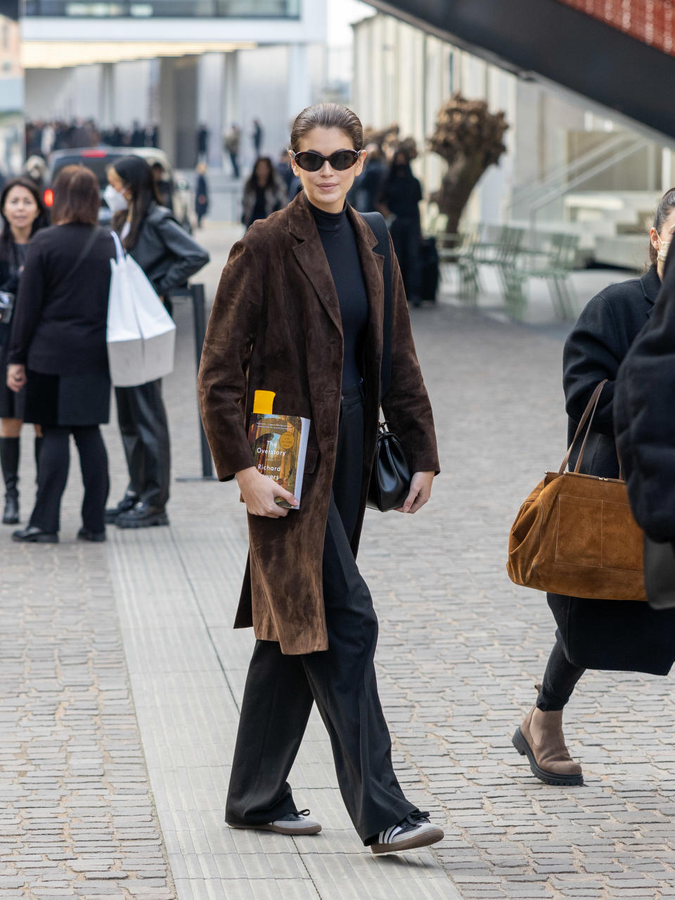 Kaia Gerber wearing a brown suede coat wtih black trousers and black Adidas Samba sneakers