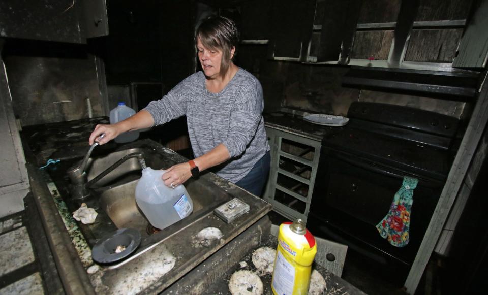 Angela Goodson fills up jugs of water for her dog in her burned out kitchen after fire ravaged thei Goodson’s home on Lunsford Drive in Kings Mountain.