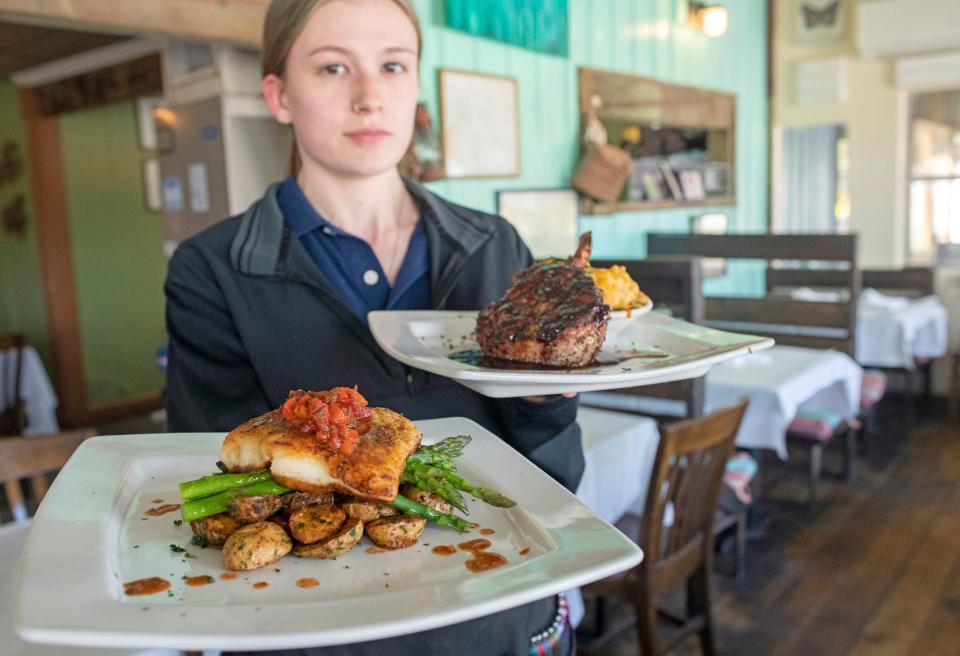 Fisherman's Corner server Sadie Warner presents two of the Perdido Key restaurant's signature dishes, a pan-seared Grouper over Asparagus and potatoes and a Bone-in pork chop with blackberry BBQ sauce. 