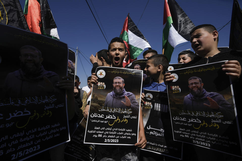 Niños palestinos ondean su bandera nacional y sostienen carteles que muestran a Khader Adnan, un miliciano palestino de Yihad Islámica que murió bajo custodia israelí tras una huelga de hambre de casi tres meses, en el pueblo cisjordano de Arrabe, cerca de Yenín, el martes 2 de mayo de 2023. El cartel en árabe dice "La Yihad Islámica en Palestina llora al amado líder Khader Adnan. El mártir de la dignidad, que murió cuanod realizaba una respetuosa huelga en su estómago vacío tras una huelga de hambre que duró 86 días". (AP Photo/Majdi Mohammed)