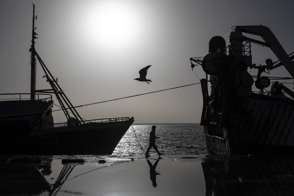 FILE - A seagull flies while a worker walks past a fishing vessel docked in the main port in Dakhla city, Western Sahara, Monday, Dec. 21, 2020. A legal adviser to the European Union’s top court has recommended that it annul Europe's fishing agreement with Morocco, which would have allowed European boats to fish for valuable catch off the coast of the disputed Western Sahara. (AP Photo/Mosa'ab Elshamy, File)