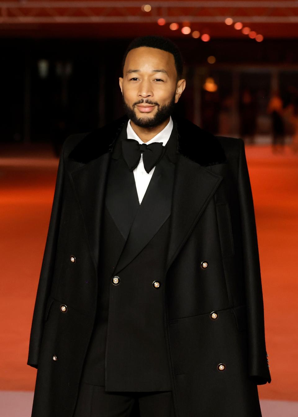 Close-up of John wearing a bow tie, suit, and coat on the red carpet