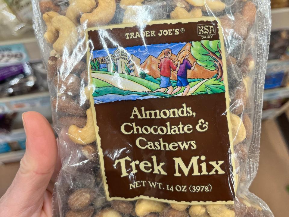 A hand holding a bag of Trader Joe's trek mix, which includes almonds, chocolate, and cashews.