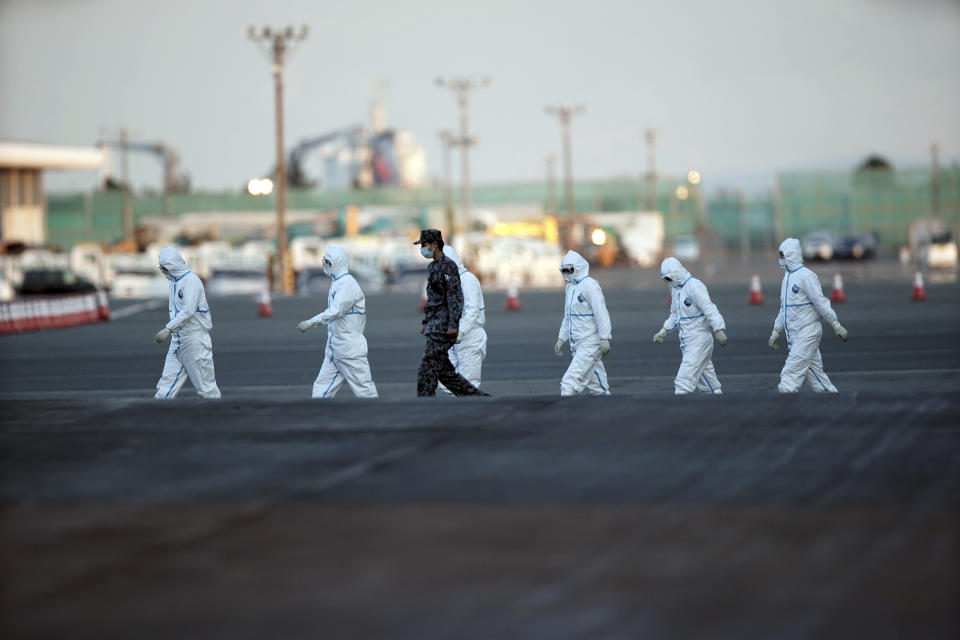 Officials with protective suites walk from the quarantined cruise ship Diamond Princess in  the Yokohama Port Monday, Feb. 10, 2020. Japan. Japan’s health ministry said Monday that about 60 more people on the quarantined cruise ship have tested positive for a new virus. (AP Photo/Eugene Hoshiko)