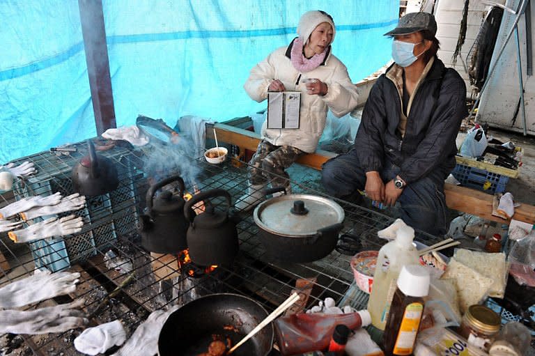 Two people chat as they prepare food while taking a break from cleaning up their destroyed shop in the devastated city of Ishinomaki. Smoke belched from a stricken nuclear plant in Japan on Monday, disrupting urgent efforts to repair the cooling systems as Tokyo halted some food shipments owing to radiation worries