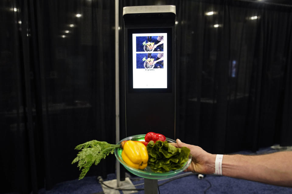 A person demonstrates the Orbisk food waste monitor during CES Unveiled, before the start of the CES tech show, Tuesday, Jan. 3, 2023, in Las Vegas. The device uses AI image recognition to track food as it is thrown away, displaying the data on a computer dashboard. (AP Photo/John Locher)