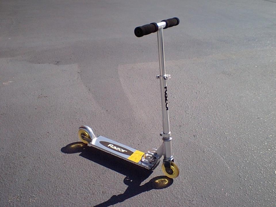 A two-wheeled handlebar scooter standing up straight on pavement. Not sure how it's standing up on its own