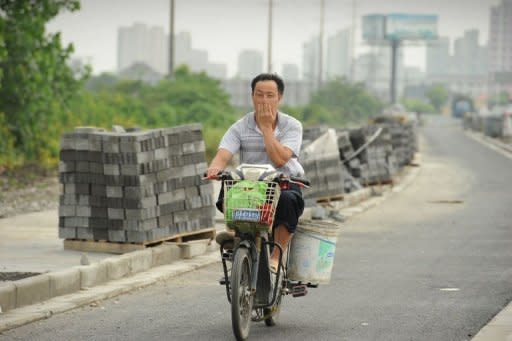 A man covers his nose against the stench rising from a garbage dump as he rides on his motorcycle in the Songjiang district of Shanghai. When the wind blows, residents can smell the stench rising from the garbage dump, feared to be so harmful it can make people vomit and cause birth defects