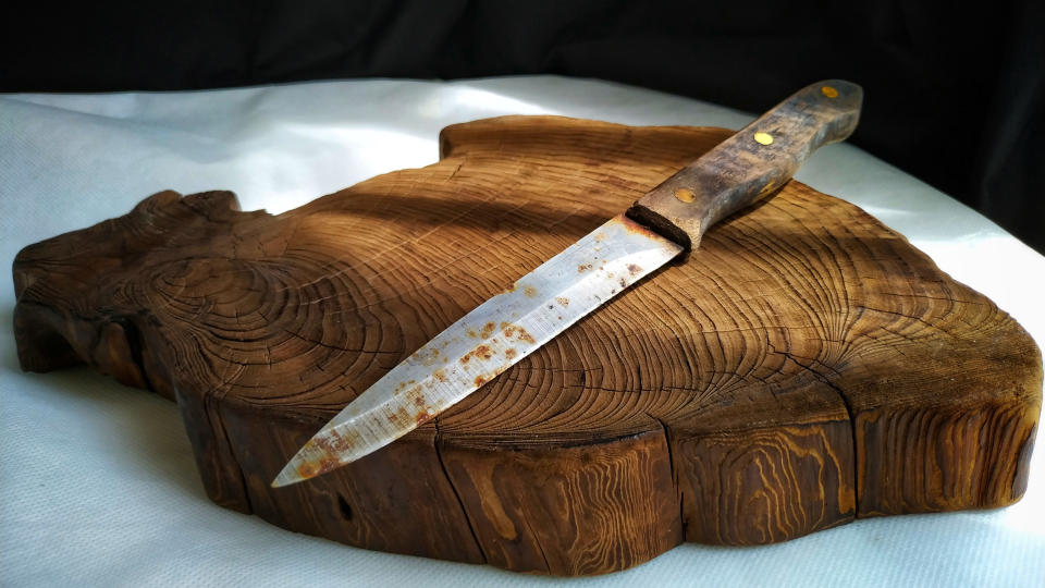 A rusty knife sitting on a wooden cutting board