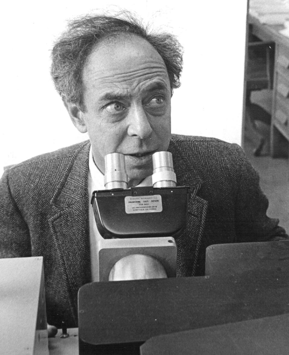 frank oppenheimer sits behind a microscope, he wears a heavy suit jacket